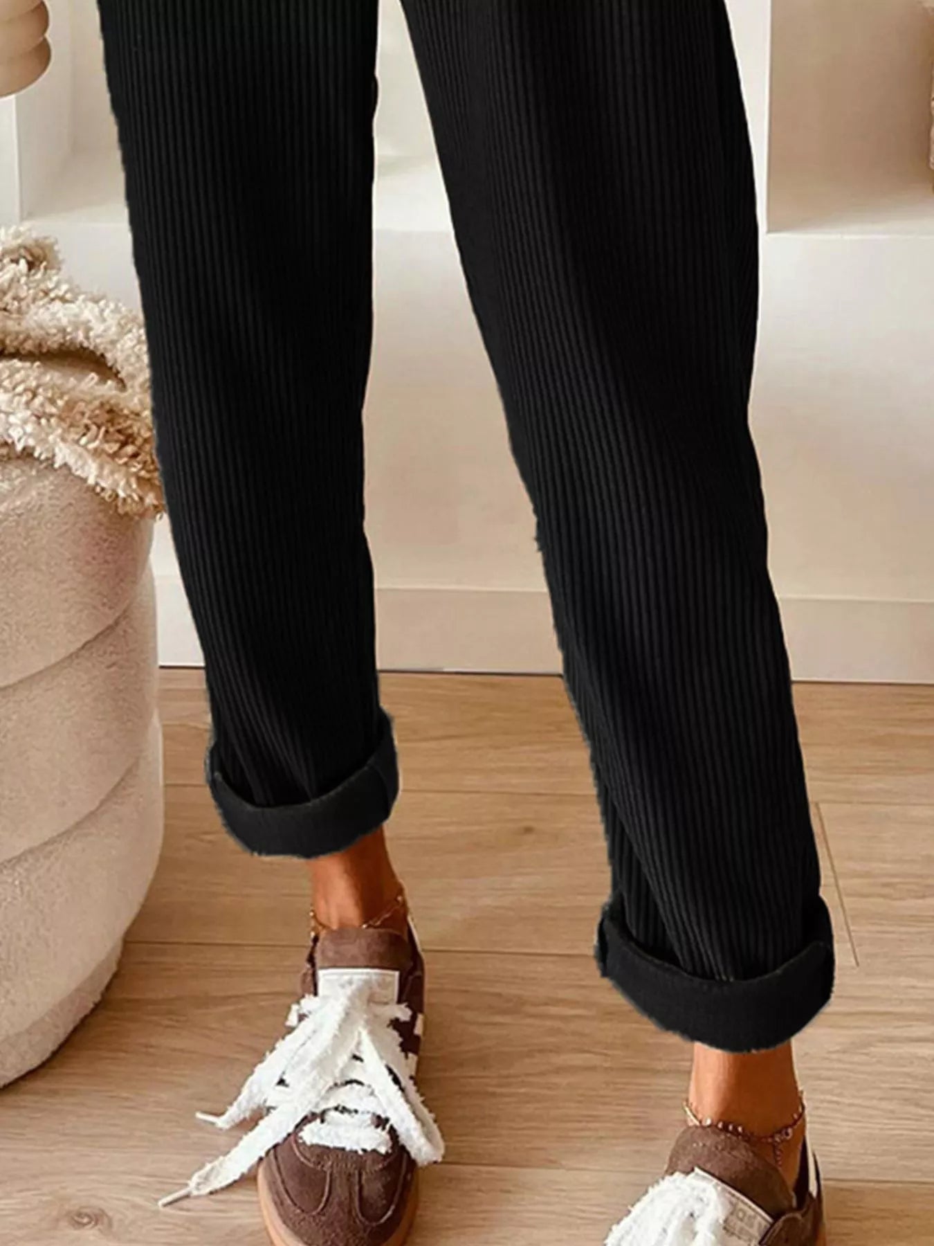 Person wearing black ribbed pants with white sneakers on a wooden floor.