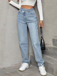 Person wearing light blue jeans and white sneakers against a gray wall.