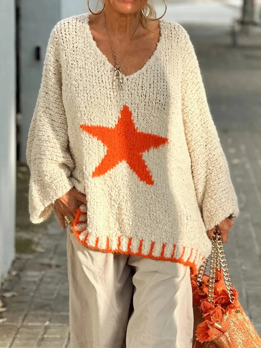 Person wearing a beige sweater with an orange star design, holding an orange bag.