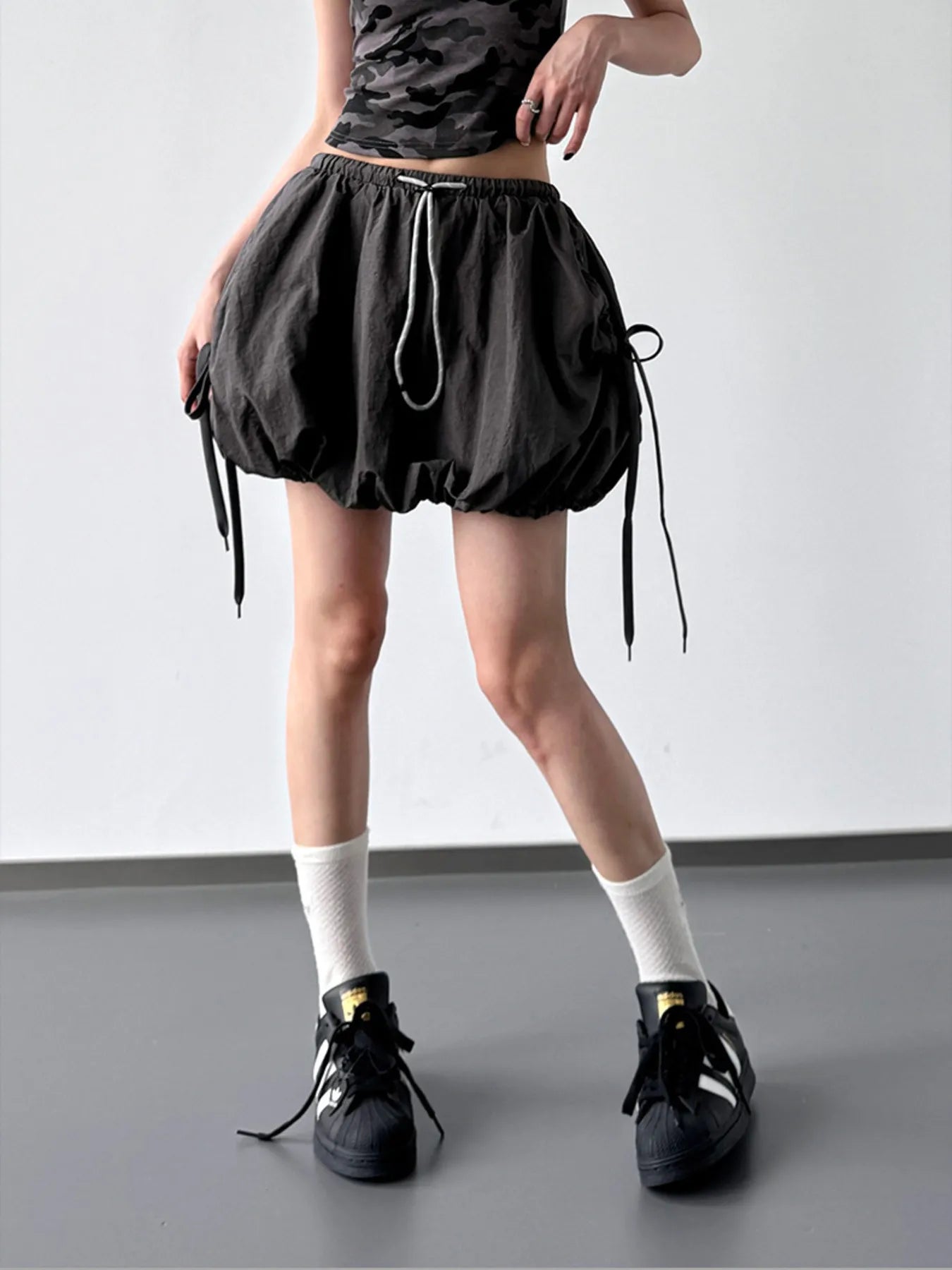Person wearing a black skirt with drawstrings on a plain background