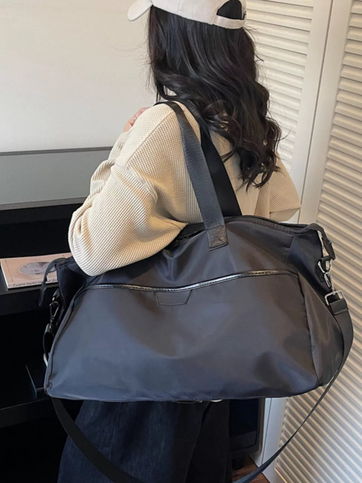 Person carrying a large black duffel bag indoors.