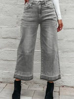 Person wearing wide-leg gray jeans against a stone wall.