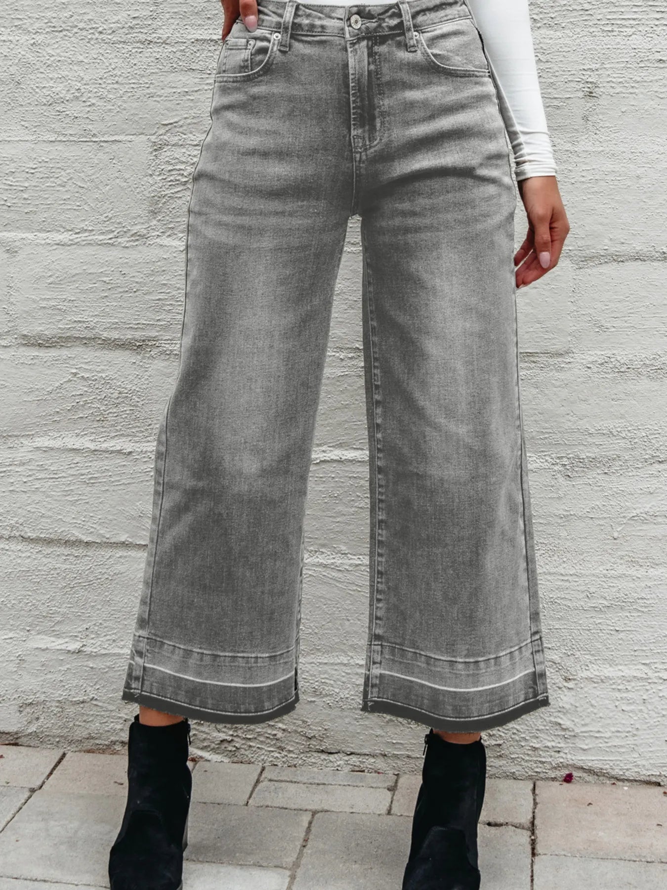 Person wearing wide-leg gray jeans against a stone wall.
