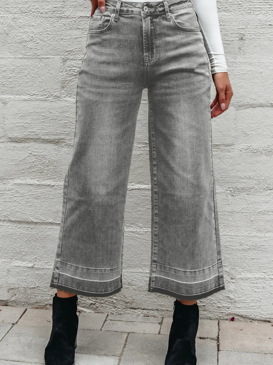 Person wearing wide-leg gray jeans against a stone wall.