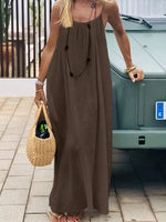 Woman in a long brown dress holding a woven bag on a tiled pavement.