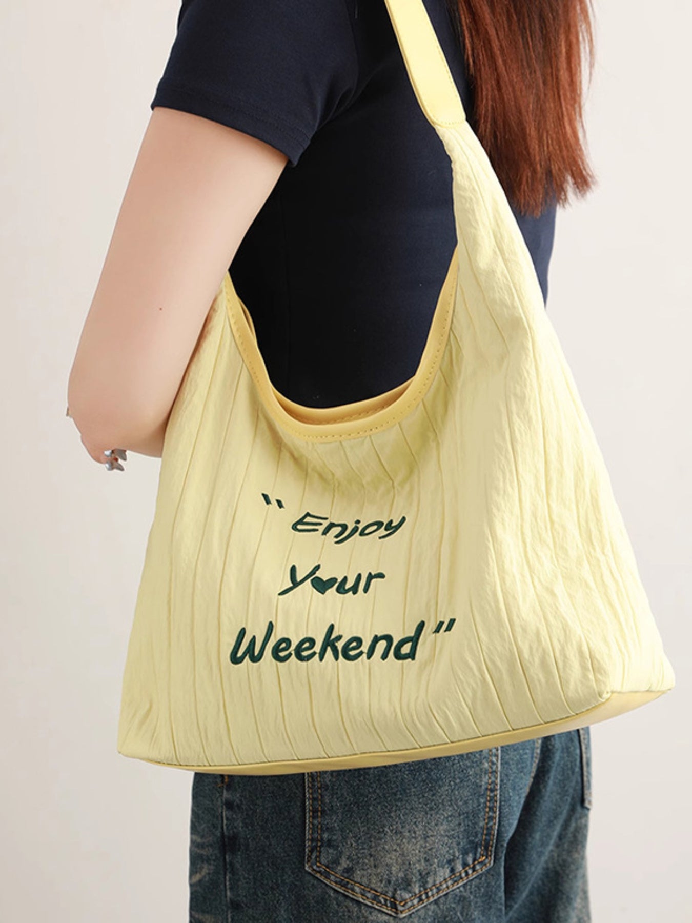 Yellow tote bag with 'Enjoy Your Weekend' text held by a person against a plain background