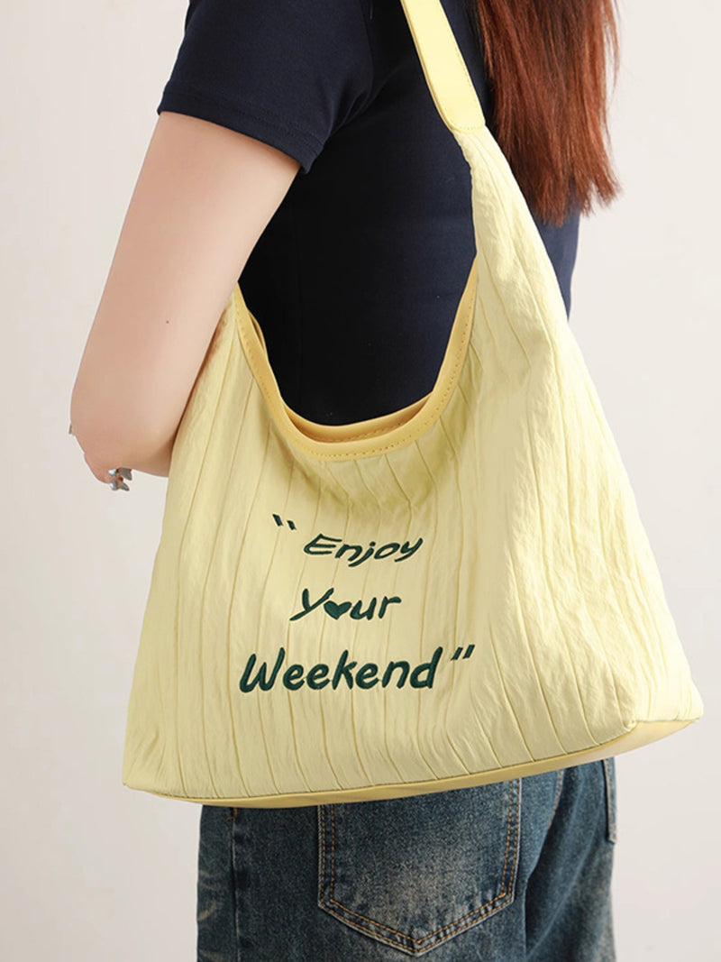 Yellow tote bag with 'Enjoy Your Weekend' text held by a person against a plain background