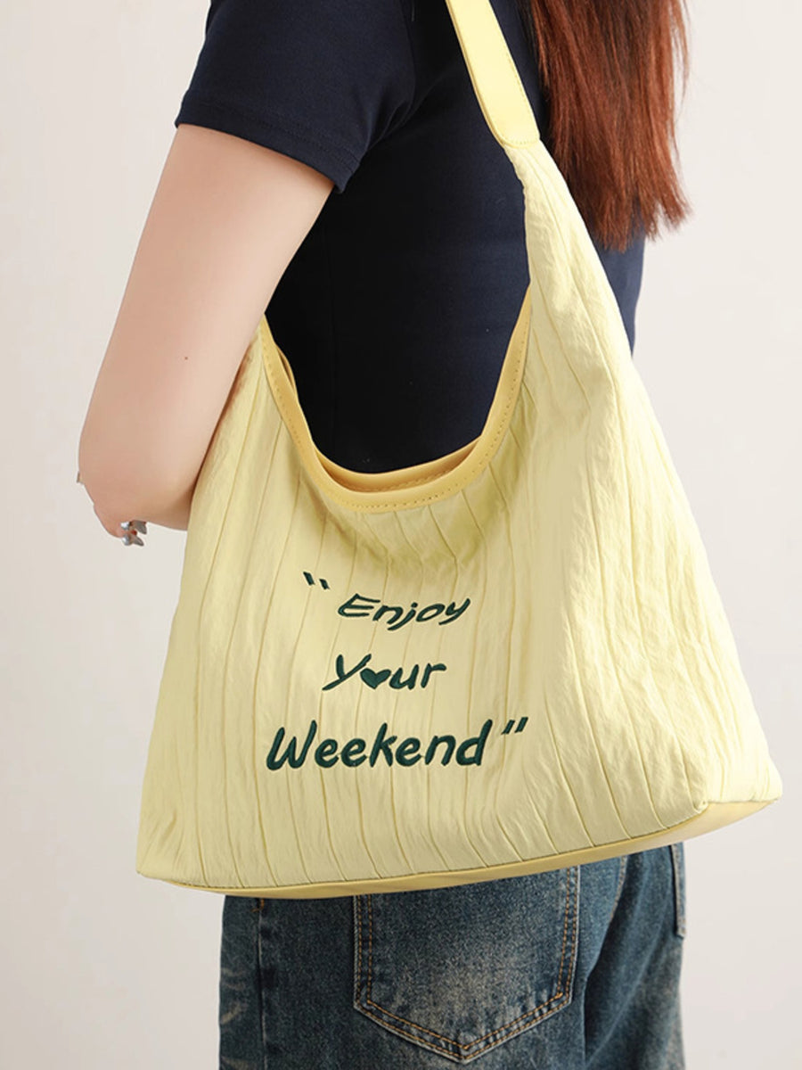 Yellow tote bag with 'Enjoy Your Weekend' text held by a person against a plain background
