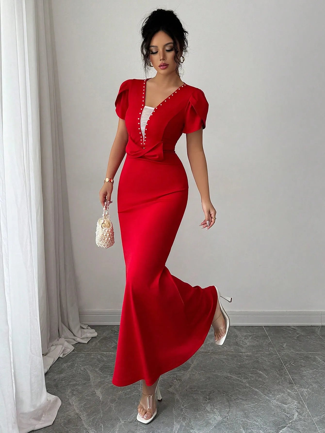 Woman in a red evening gown standing in a room with white walls and gray floor.