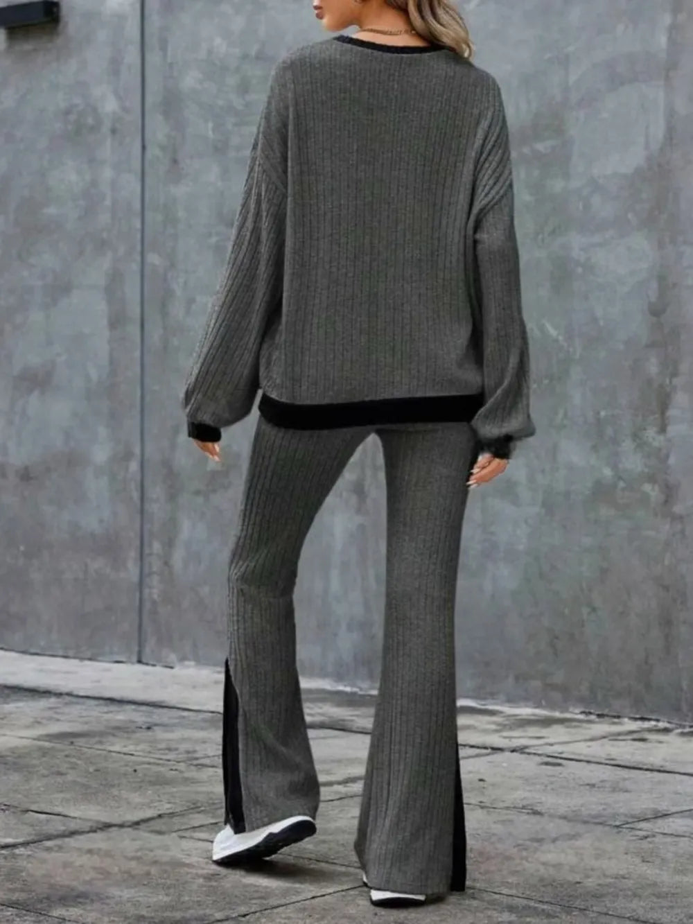 Person wearing a gray sweater and flared pants against a gray wall.