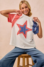 Woman wearing a colorful star-patterned top sitting on a stool against a beige background