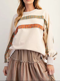 Person wearing a cream-colored sweater with patterned sleeves and a beige skirt on a white background