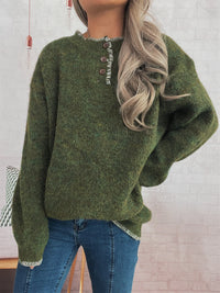 Person wearing a green sweater with button details against a light brick wall.