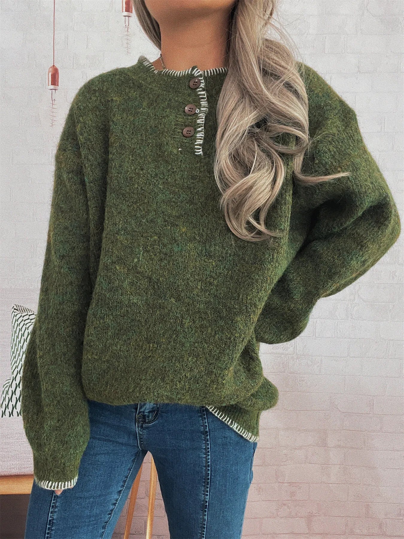 Person wearing a green sweater with button details against a light brick wall.