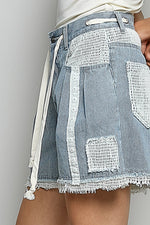 Denim shorts with white lace detailing on a plain background