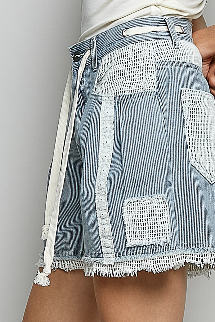 Denim shorts with white lace detailing on a plain background