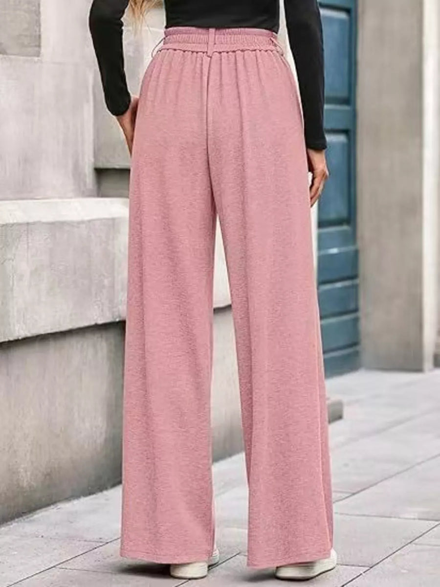 Person wearing pink wide-leg pants and a black top on a city street.
