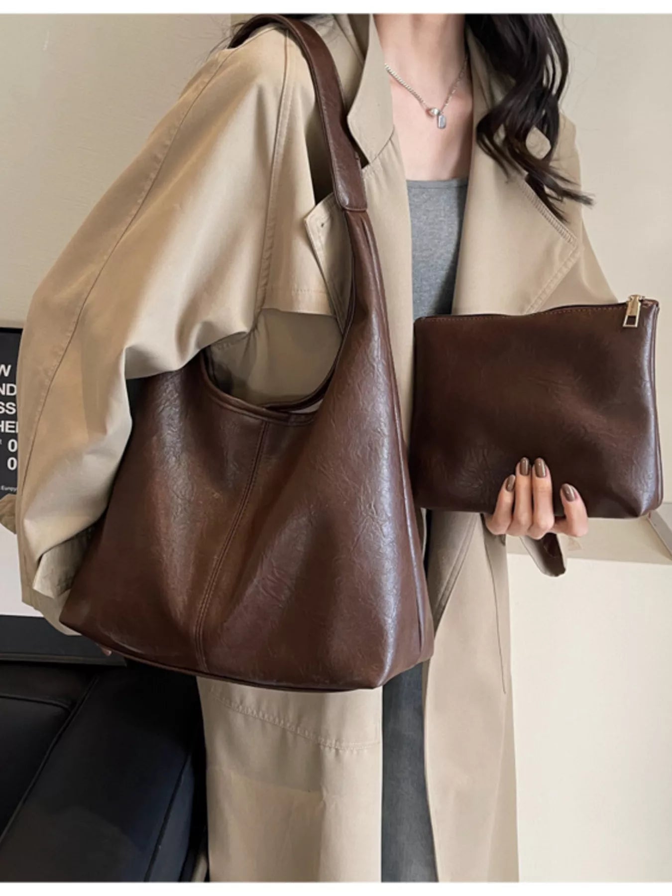 Person holding a brown leather handbag and clutch against a neutral background