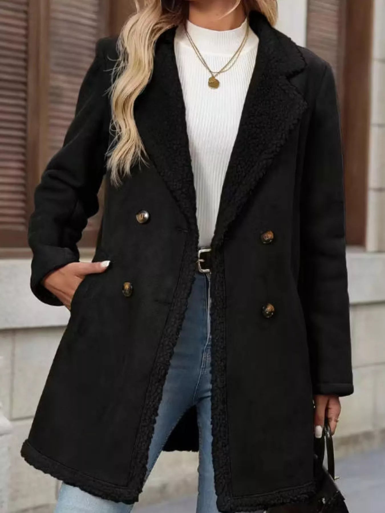 Person wearing a black coat with a white shirt and blue jeans outdoors.