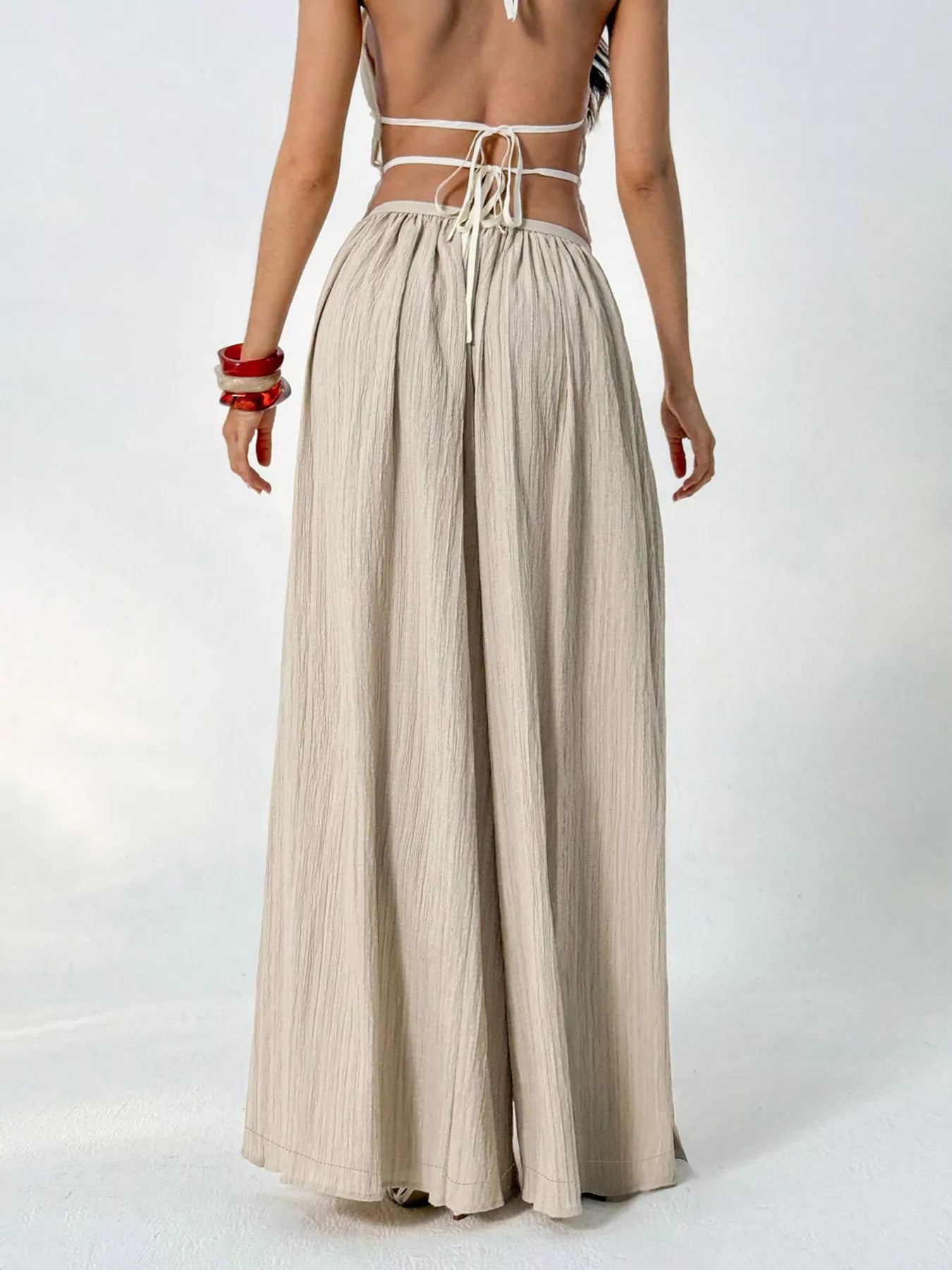 Person wearing a beige wide-leg pants and a white top with thin straps on a white background