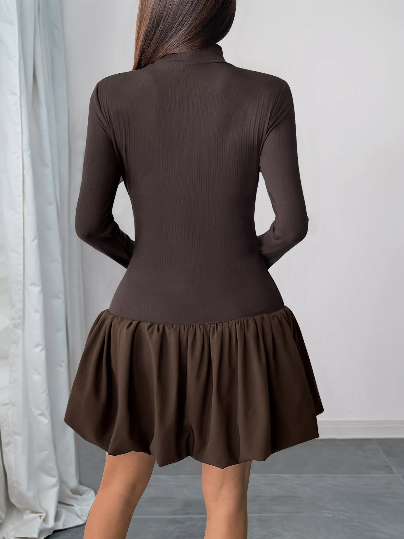 Brown dress with a ruffled skirt worn by a person against a neutral background