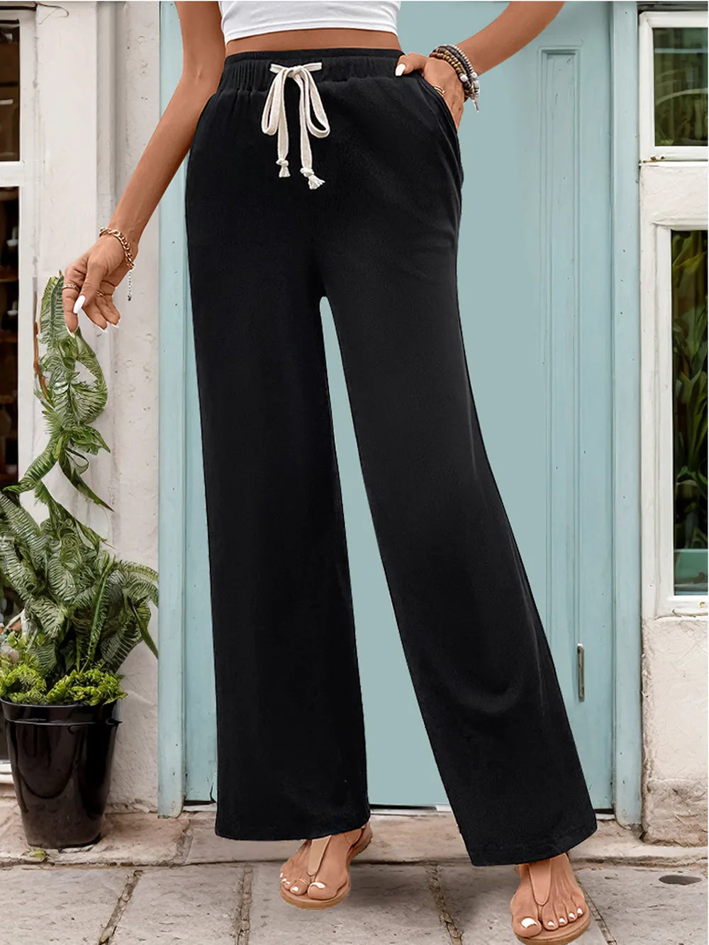 Person wearing black wide-leg pants with a drawstring in front of a light blue door.