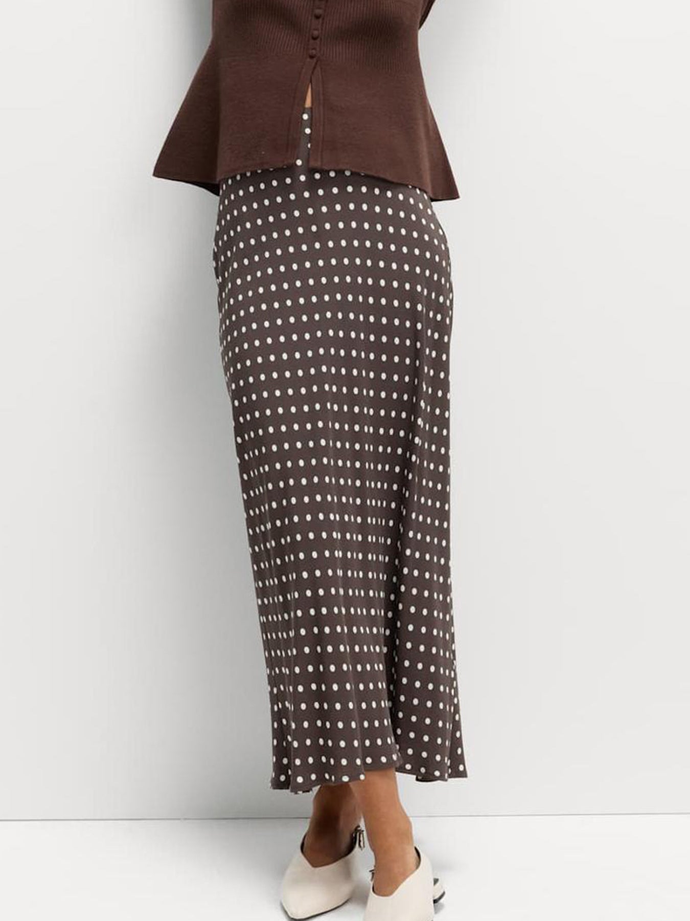 Person wearing a brown blazer and patterned skirt on a white background