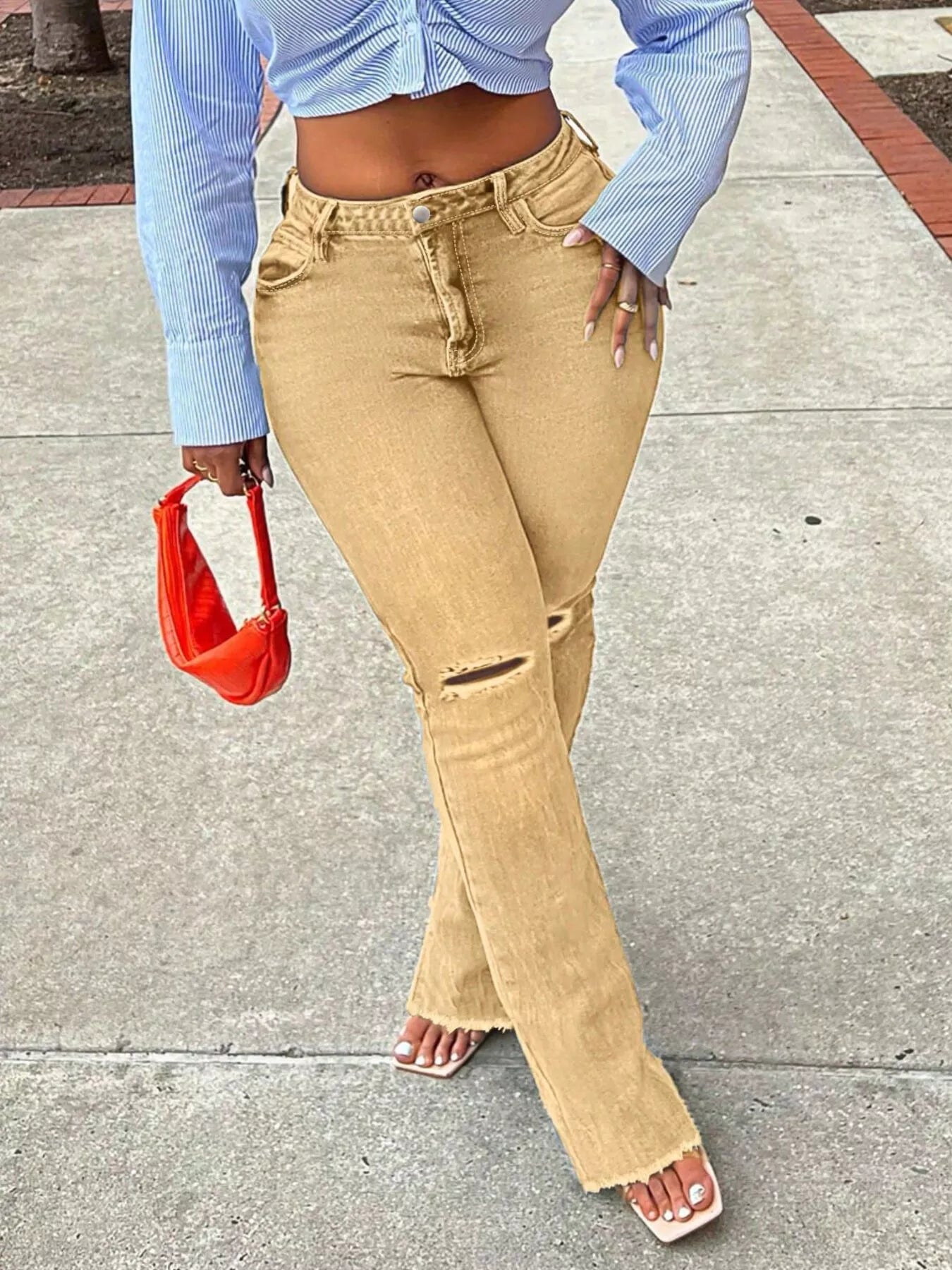 Person wearing beige flared jeans and a blue cropped top, holding an orange handbag on a sidewalk.