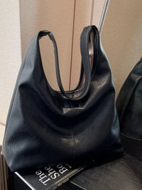 Black leather handbag on a wooden surface with a book underneath