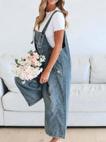 Woman wearing denim overalls holding flowers in a living room.