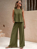 Woman wearing a green sleeveless top and wide-leg pants standing against a beige wall.