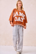 Person wearing a 'GAME DAY' oversized sweatshirt with light blue jeans on a plain background