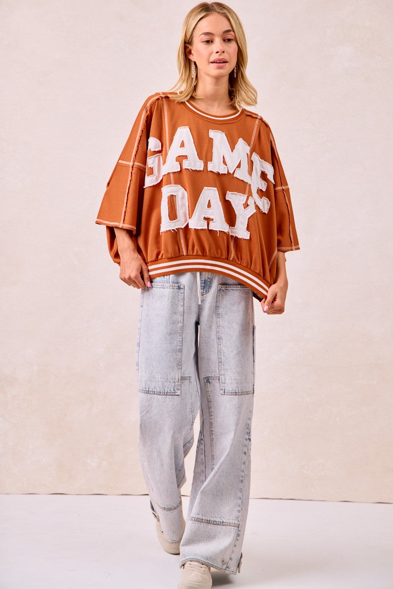 Person wearing a 'GAME DAY' oversized sweatshirt with light blue jeans on a plain background