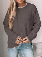 Person wearing a gray sweater with white trim and blue jeans against a neutral background