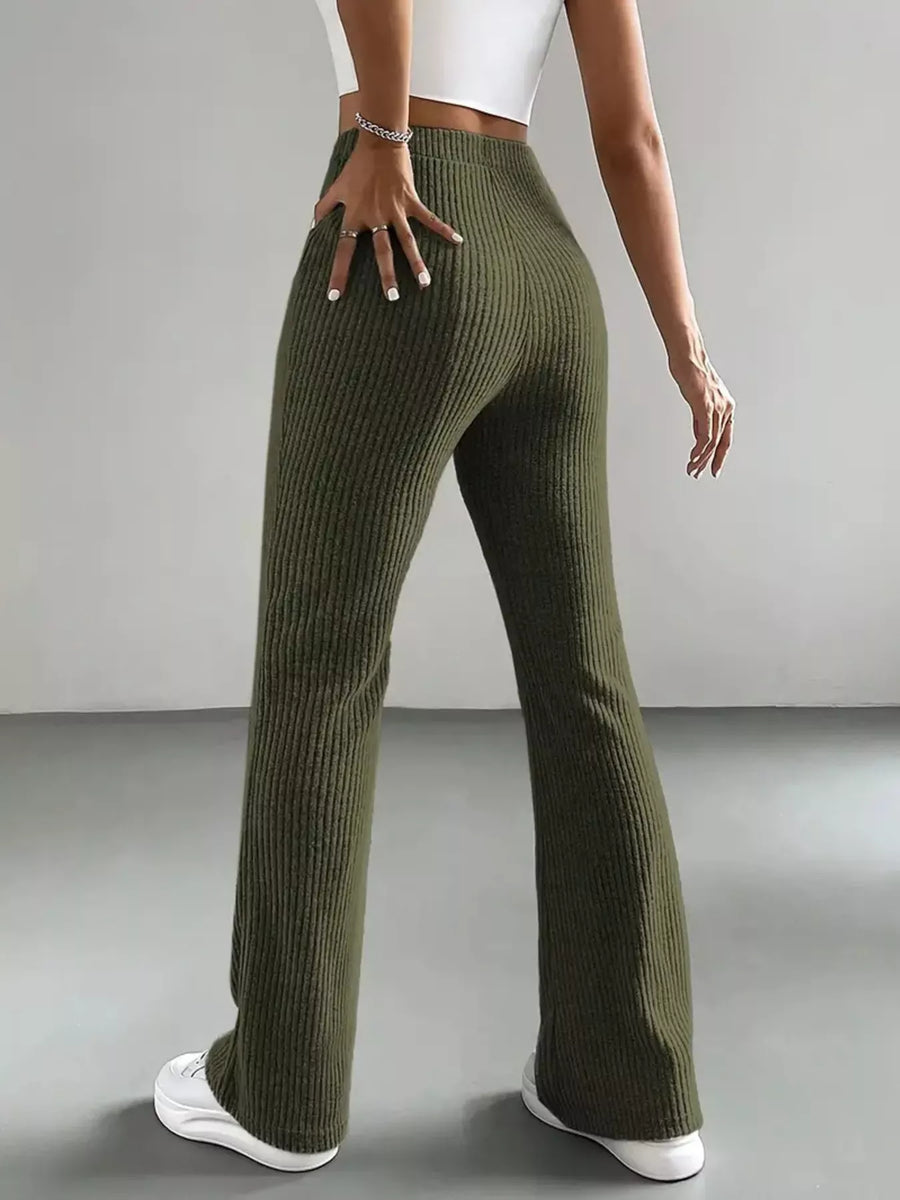 Person wearing green ribbed pants and white sneakers on a plain background