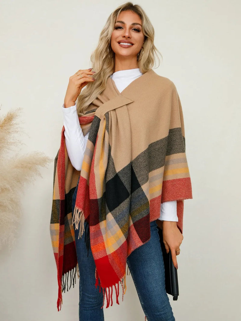 Woman wearing a beige poncho with a plaid pattern over a white shirt and blue jeans.