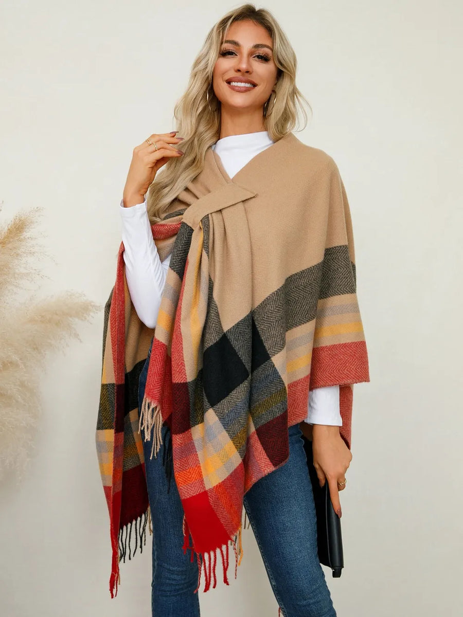 Woman wearing a beige poncho with a plaid pattern over a white shirt and blue jeans.