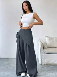 Woman wearing a white top and gray wide-leg pants in a minimalistic room.