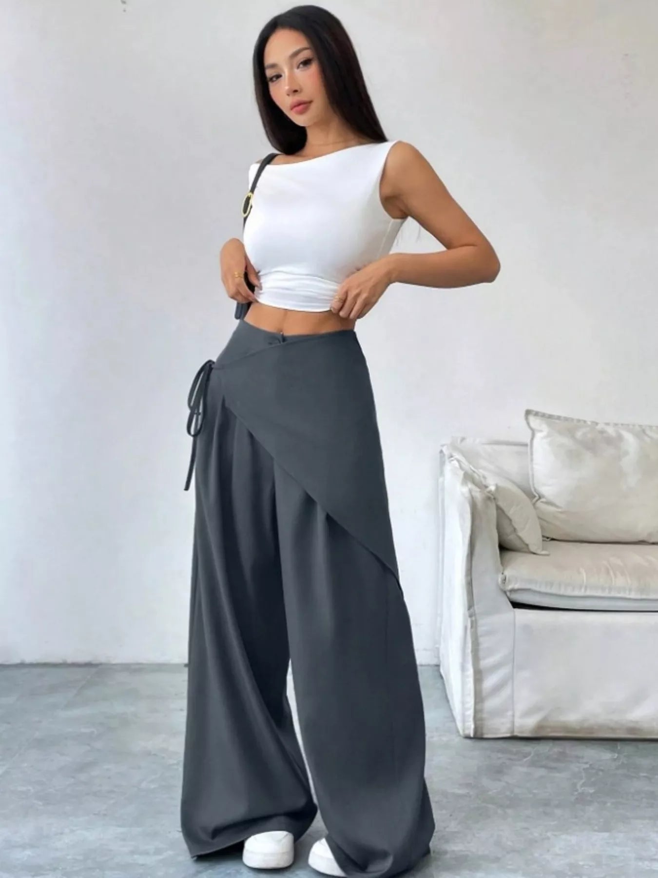 Woman wearing a white top and gray wide-leg pants in a minimalistic room.