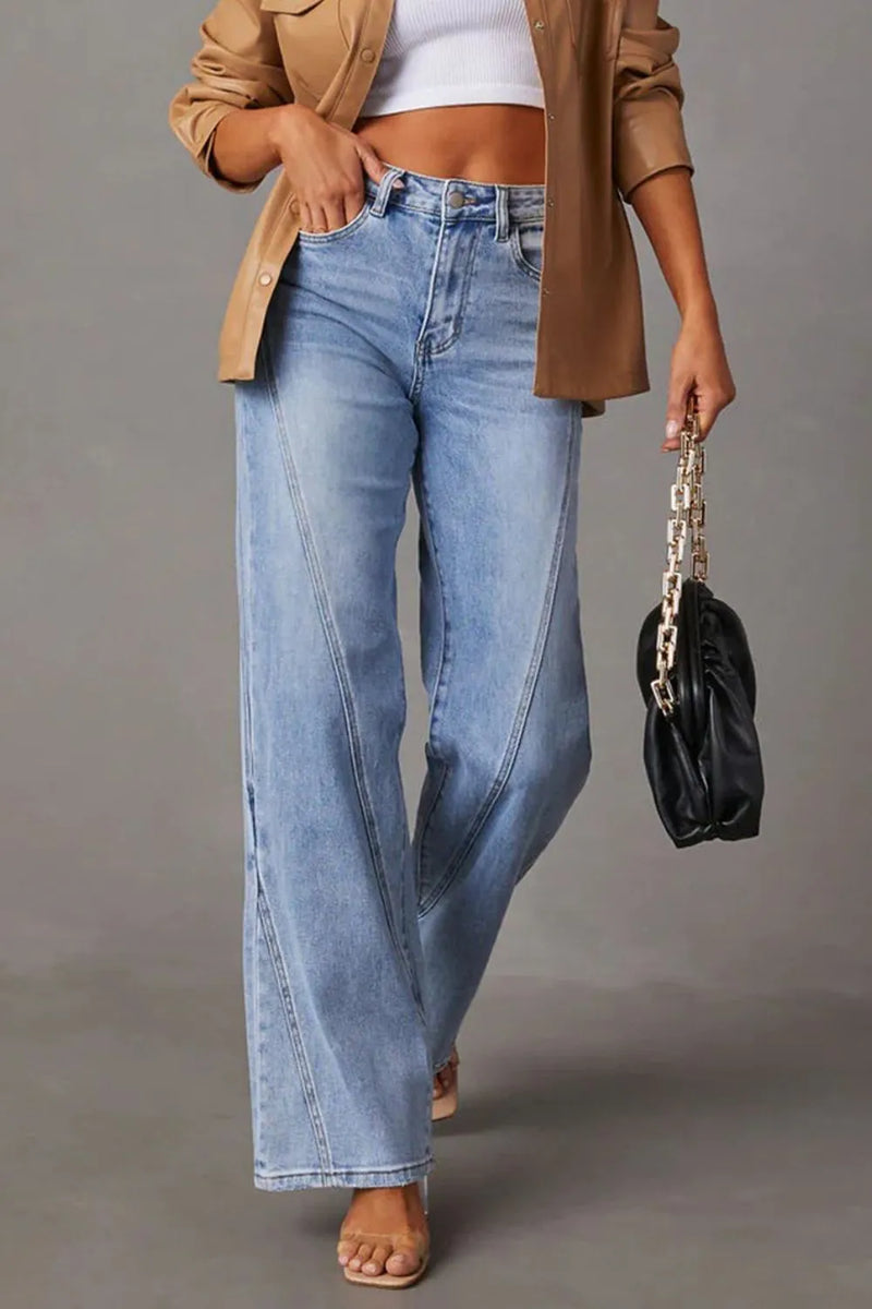 Person wearing light blue jeans and a beige jacket, holding a black handbag on a gray background