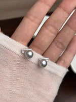 Silver earrings being worn on a finger against a neutral background