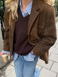 Person wearing a brown coat, dark sweater, and blue jeans, holding a coffee cup.