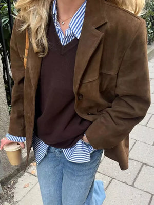 Person wearing a brown coat, dark sweater, and blue jeans, holding a coffee cup.