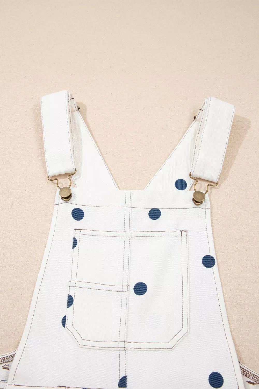 White denim overalls with blue polka dots on a beige background
