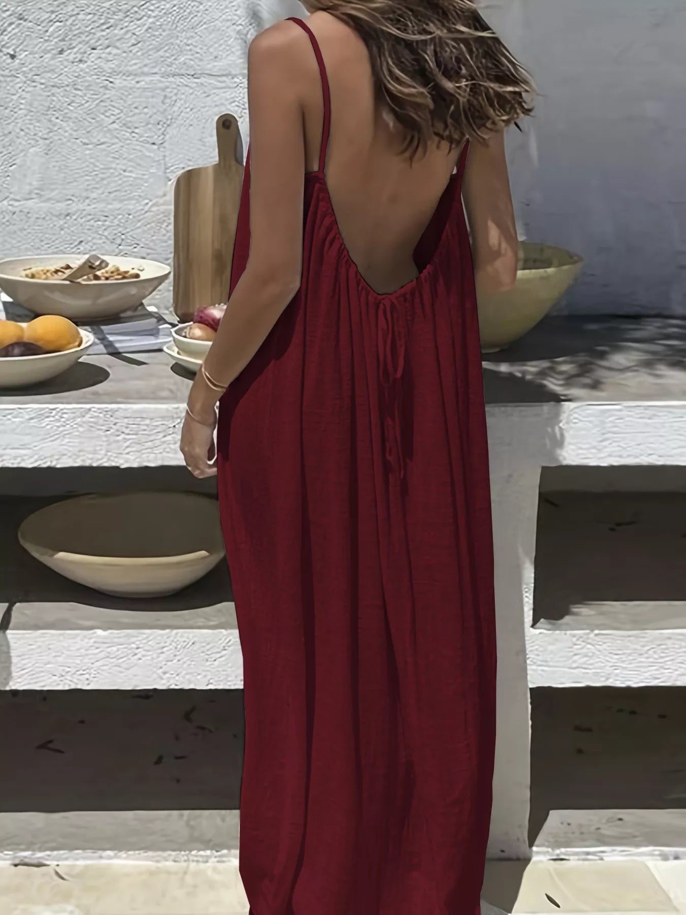 Woman in a red dress standing on outdoor steps with a white wall and wooden table in the background.