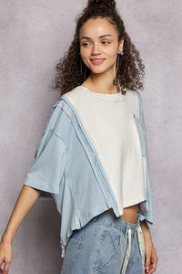 Woman wearing a light blue jacket over a white shirt with jeans against a gray background
