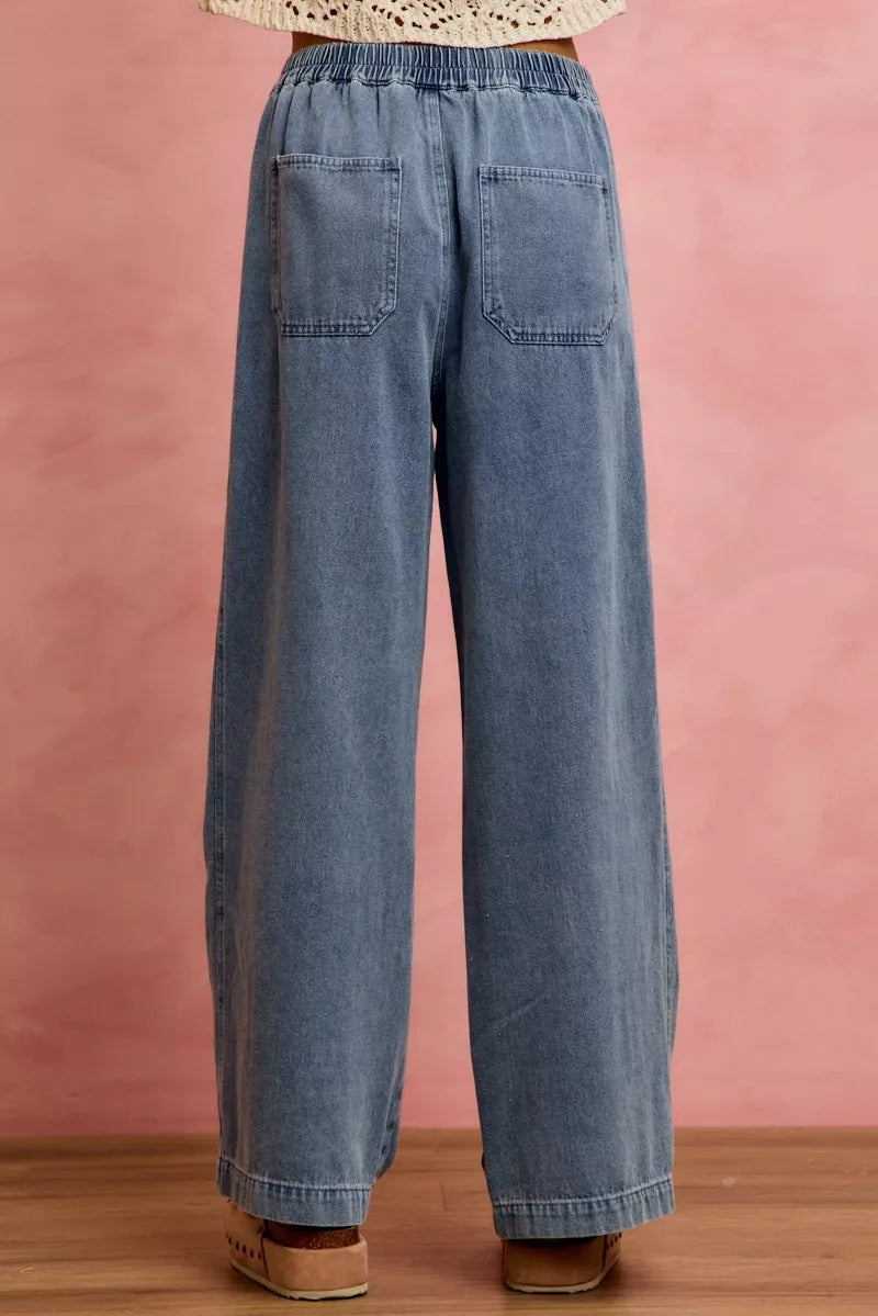 Blue wide-leg jeans worn by a person against a pink background