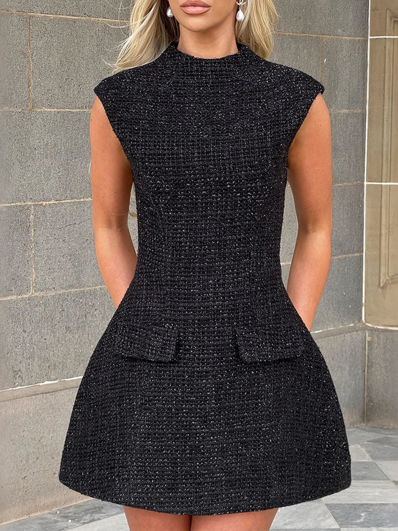 Black dress worn by a model against a stone wall background