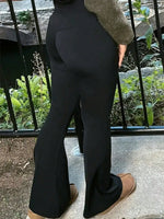 Person wearing black flared pants standing outdoors with a garden background