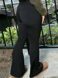 Person wearing black flared pants standing outdoors with a garden background